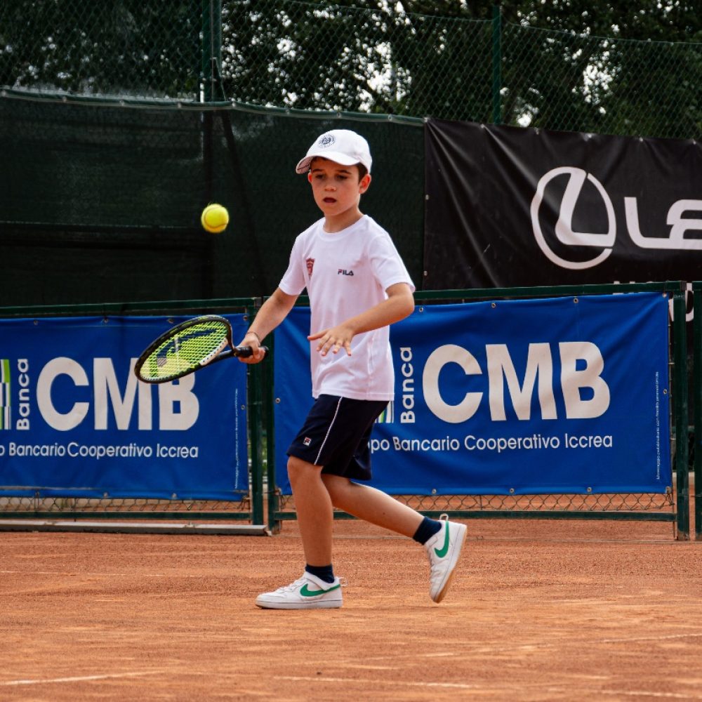 Bambino con cappellino bianco che segue la palla preparando il dritto su campo in terra rossa al corso di tennis dell'Adriano Panatta Racquet Club di Treviso