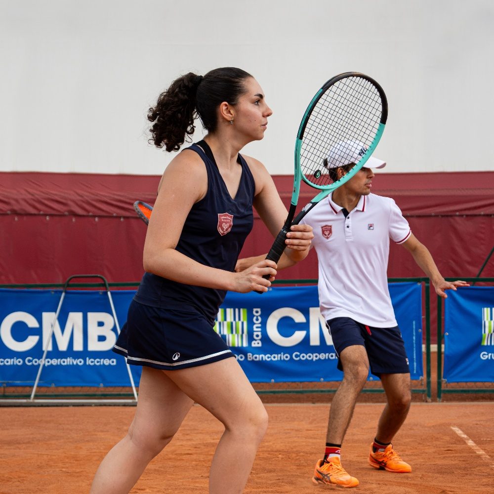 Coppia di tennisti con la divisa del club durante una partita di doppio su campo in terra rossa all'Adriano Panatta Racquet Club di Treviso