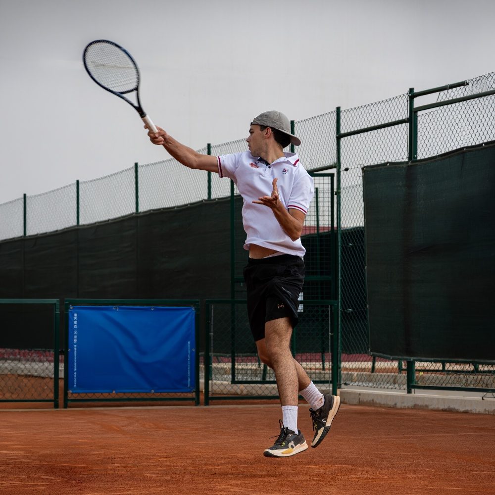 Tennista in salto mentre esegue un dritto su un campo in terra rossa dell'Adriano Panatta Racquet Club di Treviso