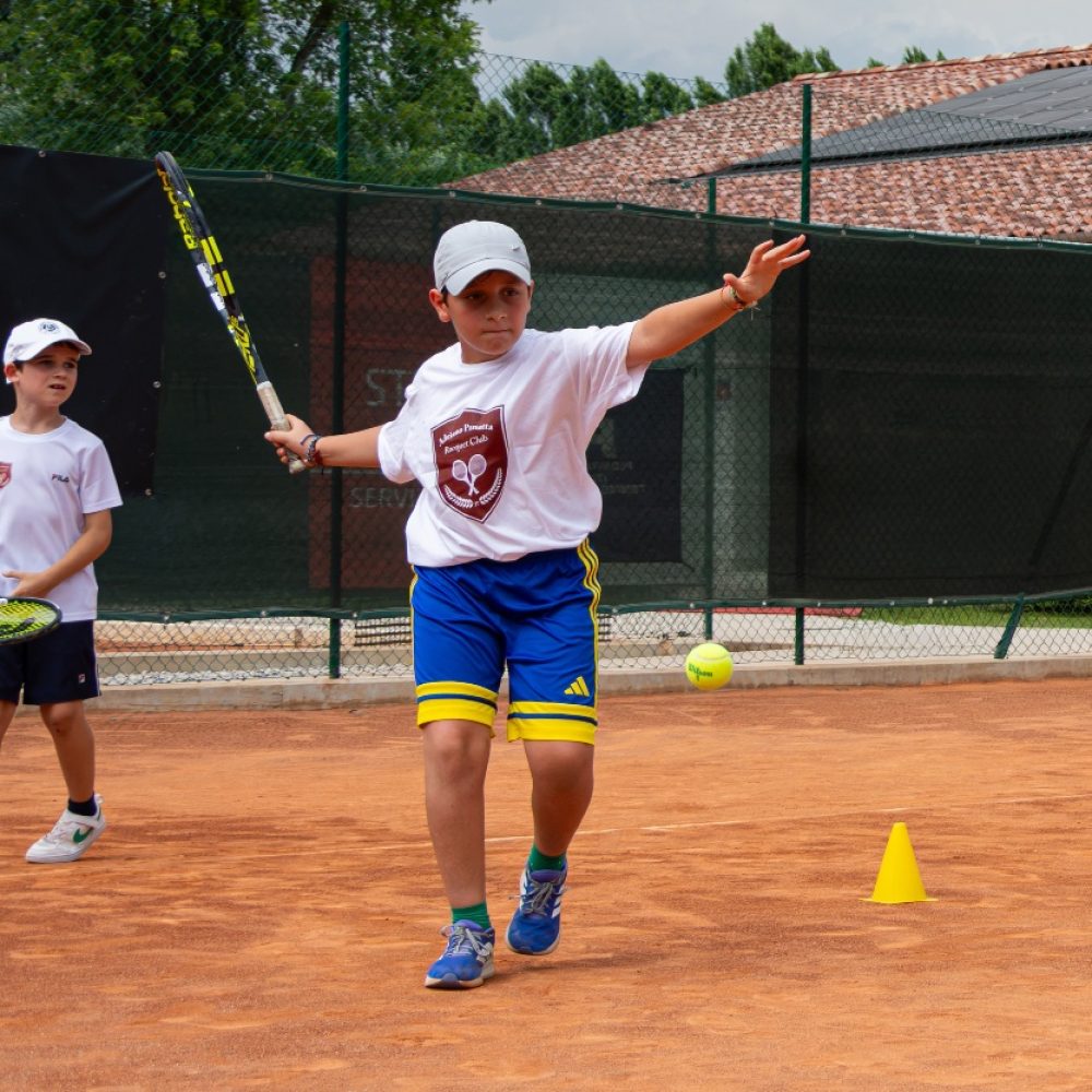Bambino con maglia del club che esegue un dritto durante un esercizio con i coni al corso di tennis dell'Adriano Panatta Racquet Club di Treviso