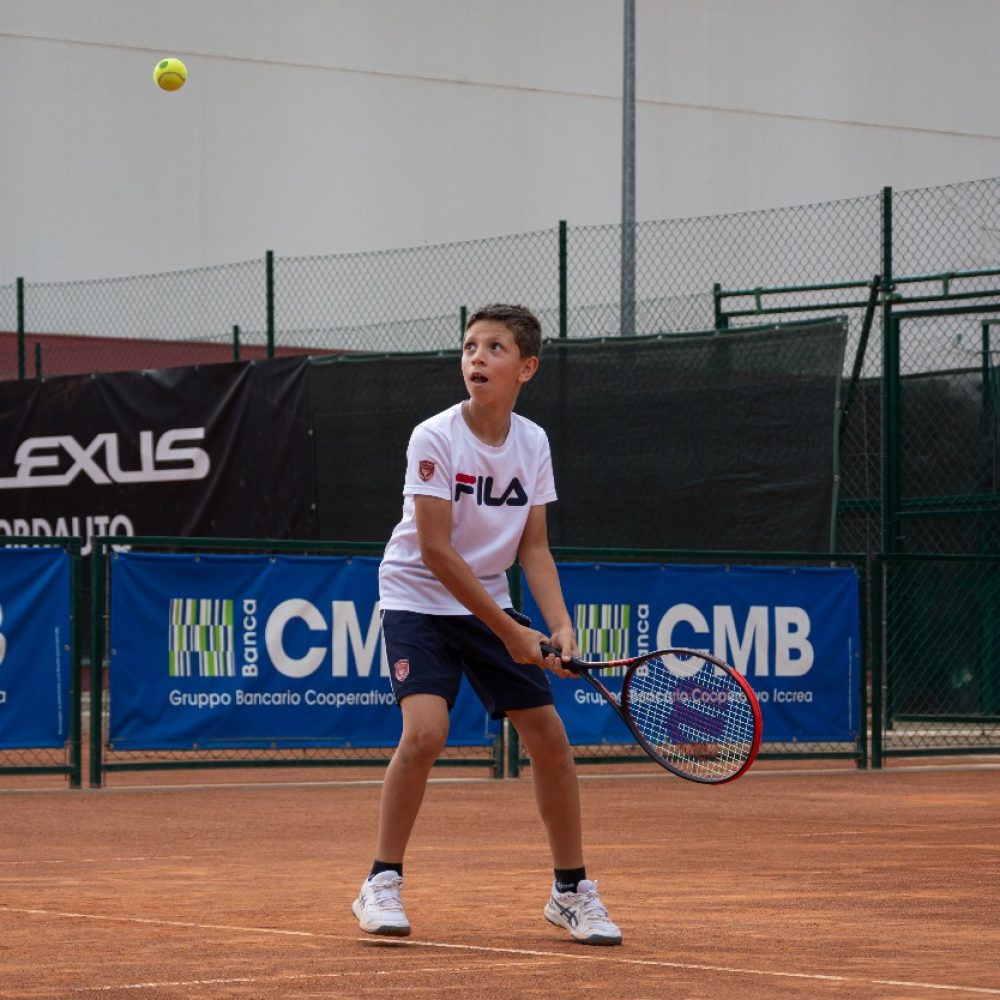 Bambino con maglia bianca che segue con lo sguardo una palla alta durante il corso di tennis all'Adriano Panatta Racquet Club di Treviso