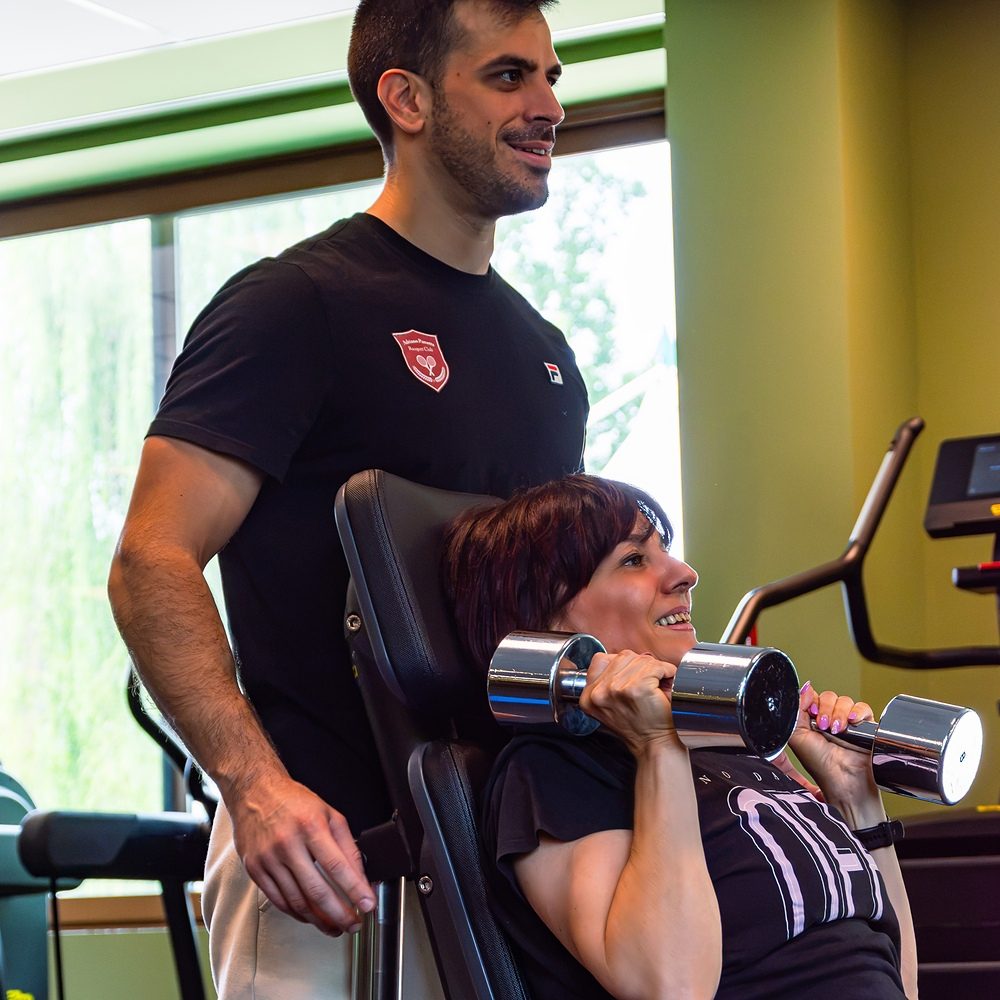 Personal trainer assiste una cliente durante un esercizio su panca con manubri a Treviso