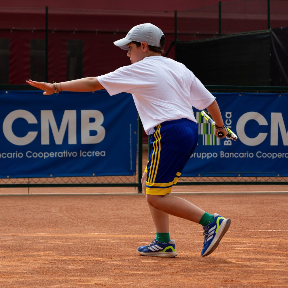 Giovane tennista con cappellino grigio in fase di preparazione del dritto su campo in terra rossa della scuola tennis FITP a Treviso