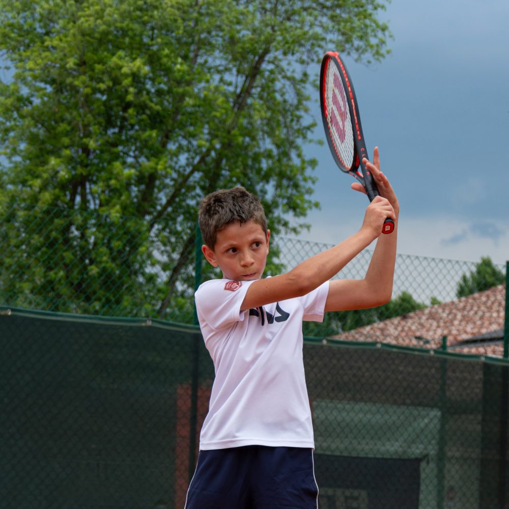 Ragazzo con maglia bianca in preparazione del rovescio a due mani durante l'allenamento della scuola tennis FITP a Treviso