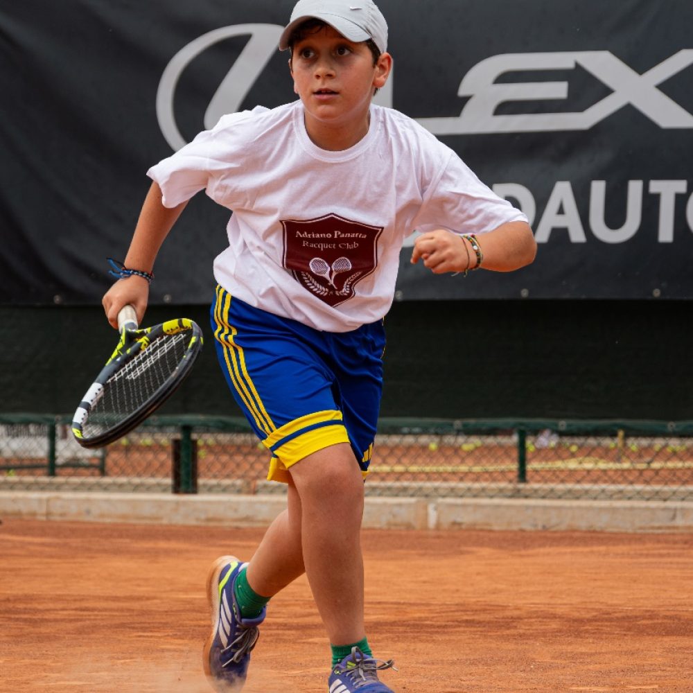 Bambino con maglia dell'Adriano Panatta Racquet Club che corre in campo con la racchetta durante il corso di tennis a Treviso