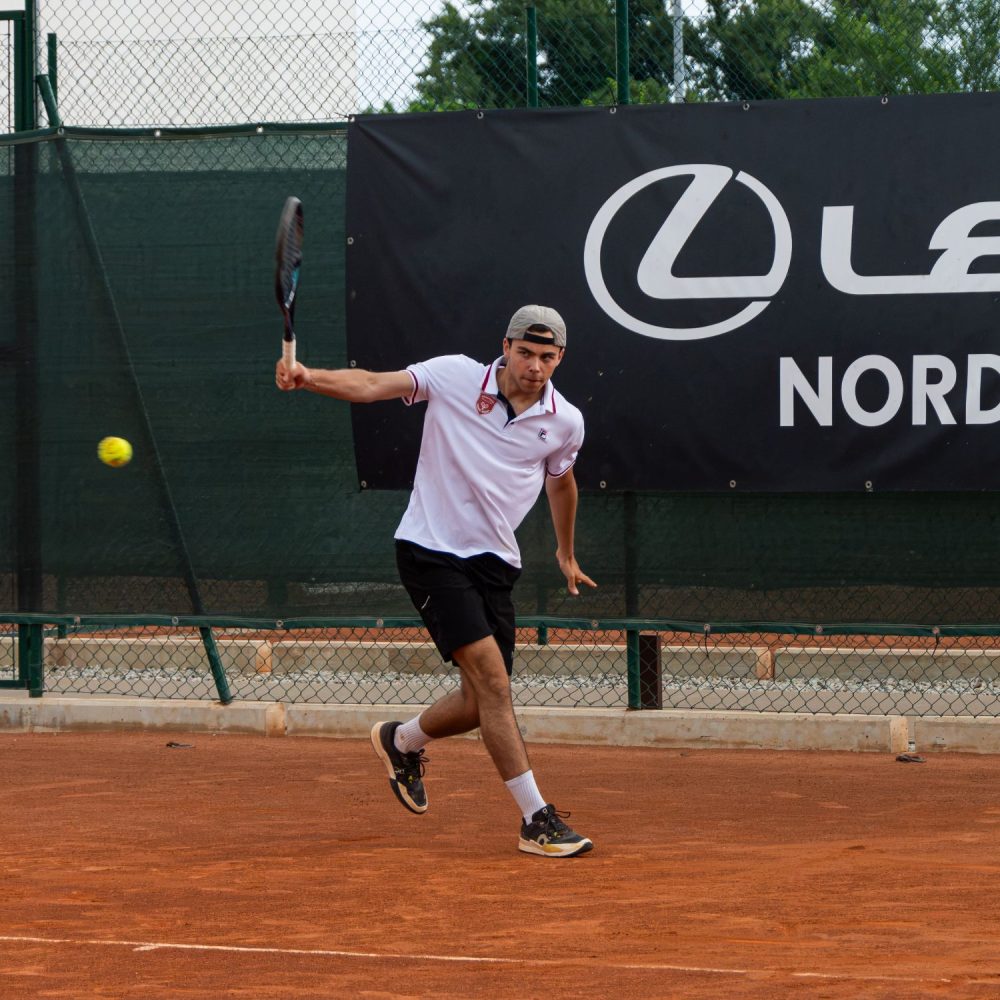 Tennista con polo bianca del club durante un colpo da fondo campo su terra rossa all'Adriano Panatta Racquet Club di Treviso