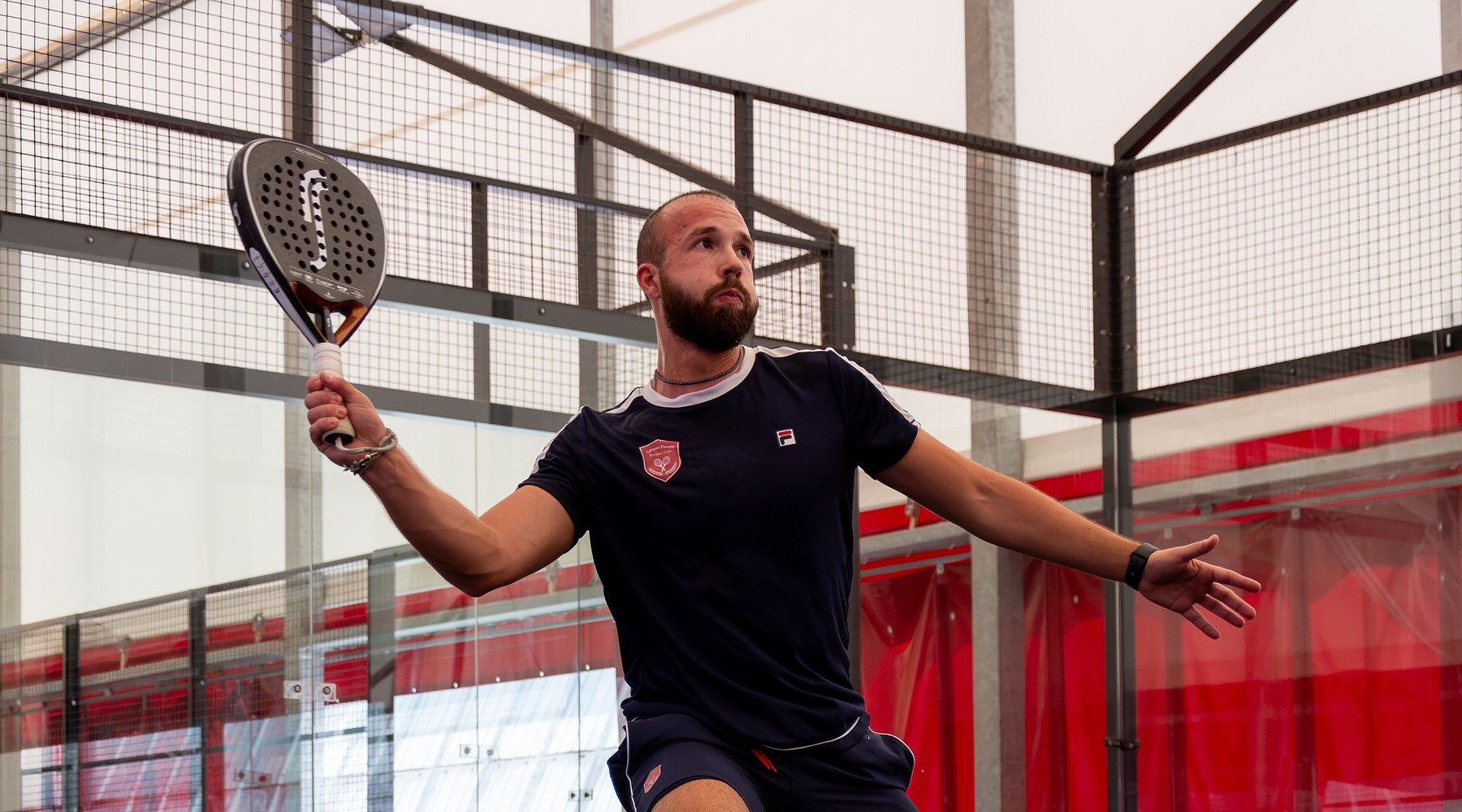 Giocatore di padel colpisce una volée alta durante una partita sul campo indoor a Treviso