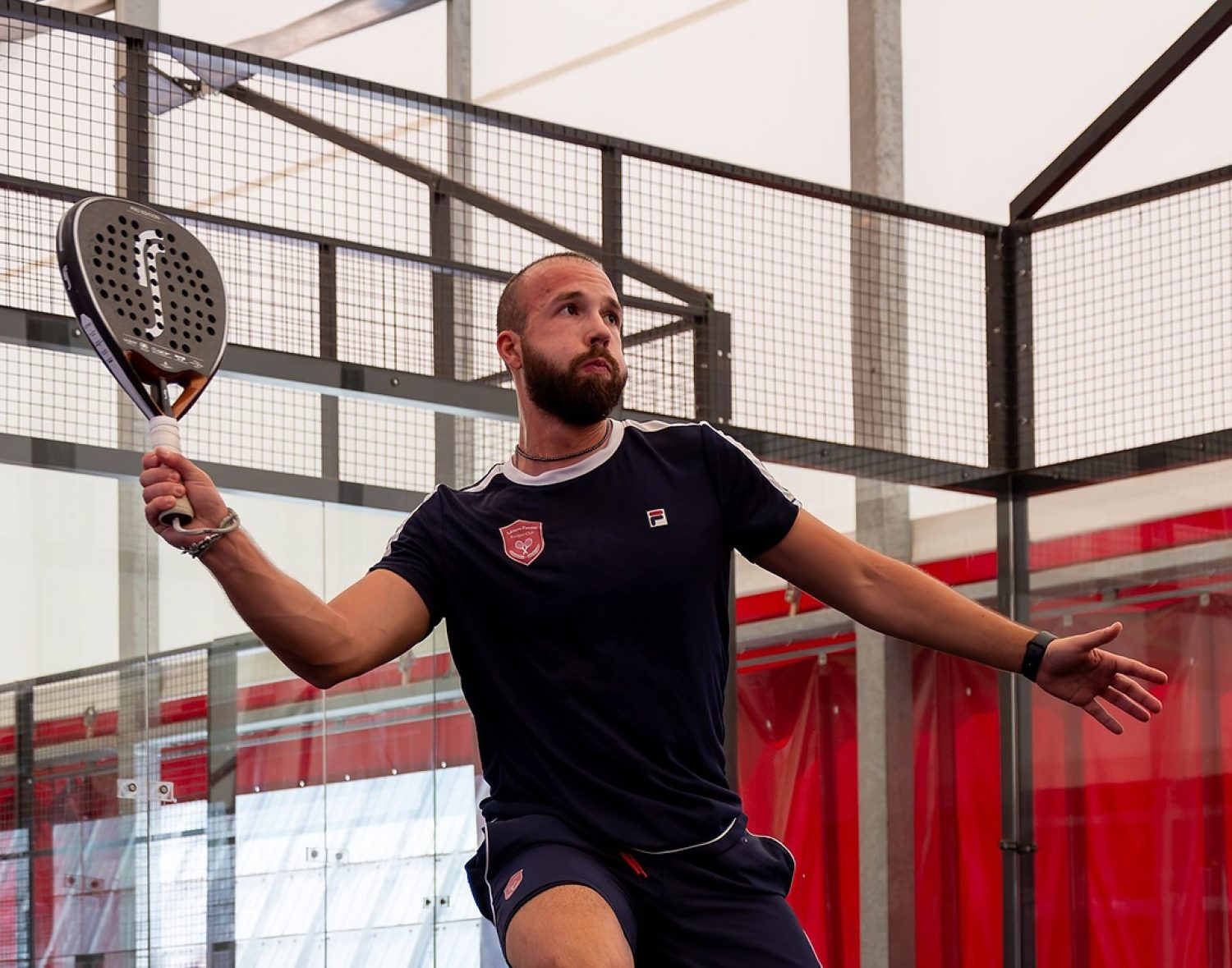 Giocatore di padel colpisce una volée alta durante una partita sul campo indoor a Treviso